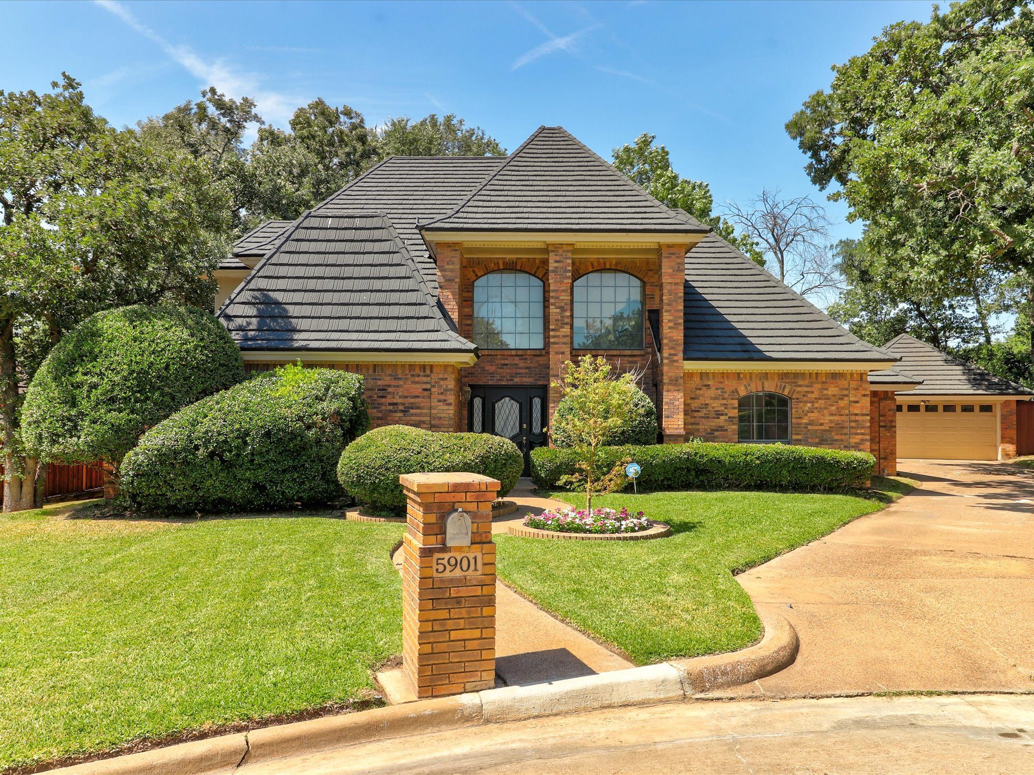 A two-story brick home with a tile roof on a green corner lot, one of Paul Ruth's listings
